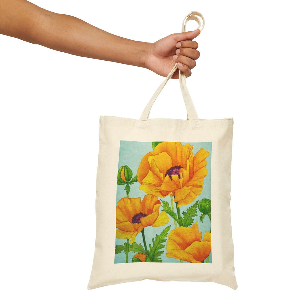 A cream-colored canvas tote bag with a colorful print of yellow poppies on a light blue background, held by a person's arm against a plain white background.