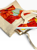 A beige canvas tote bag with a large print of red and orange poppies on the front, shown holding notebooks and books on a white background.