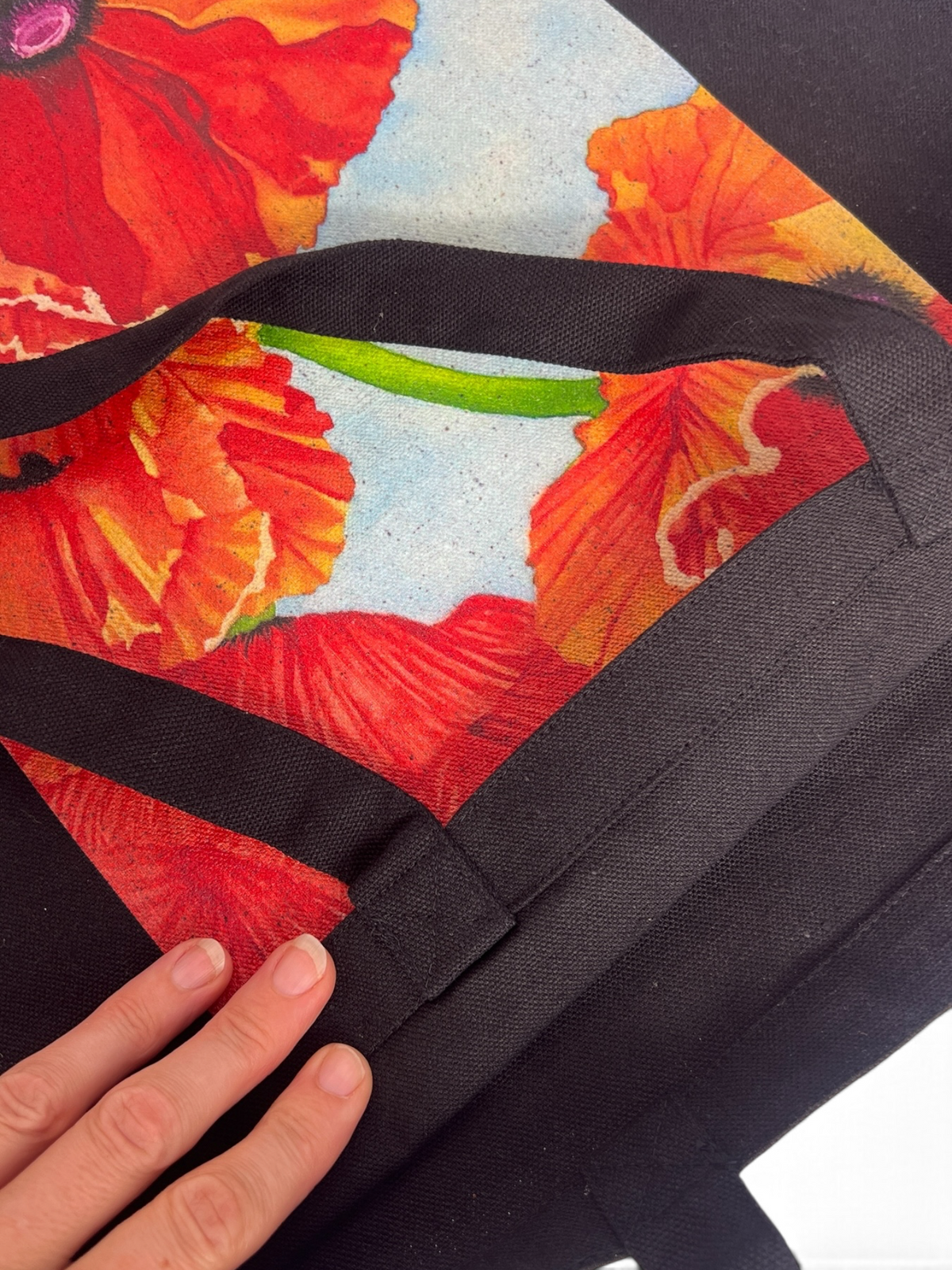 Close-up of red poppy watercolor print on black canvas, showing fabric texture and dark flecks